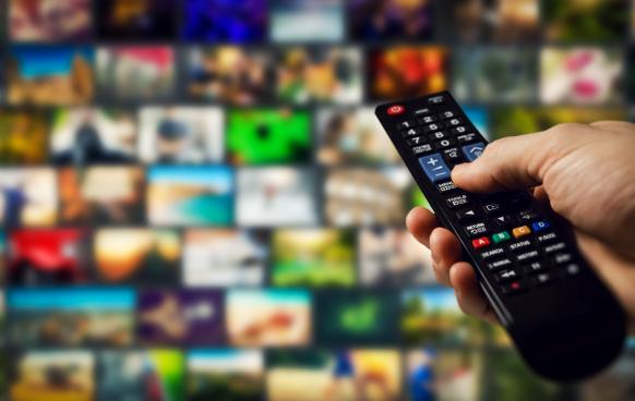 Hand holding a remote control in front of a variety of TV shows