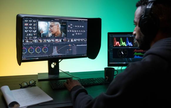 Photo of a man at a computer workstation color grading video footage in DaVinci Resolve. Photo by Ron Lach