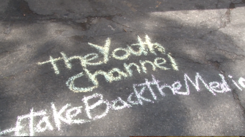 Concrete ground with chalk letters: "The youth Channel #TakeBackTheMedia"