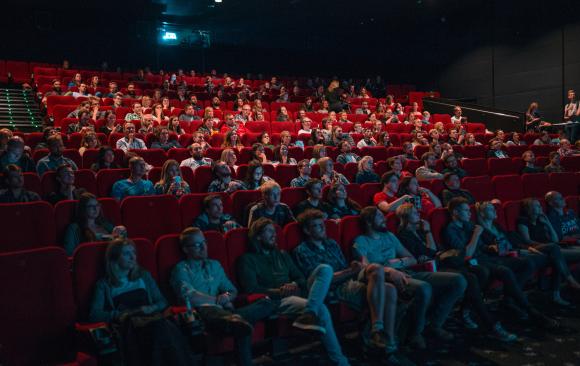 Photograph of a large group of people in a theater looking towards an unseen movie screen. Photo by Krists Luhaers on Unsplash