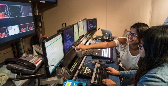 Woman next to peer pointing at screen in control room.