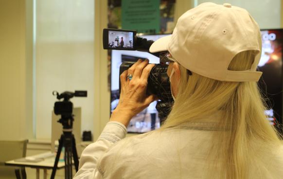 Woman in a hat adjusts the zoom on a Sony Z150 video camera in a classroom.