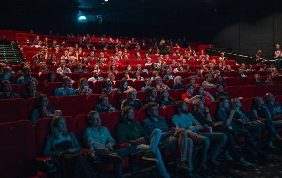 Photograph of a large group of people in a theater looking towards an unseen movie screen. Photo by Krists Luhaers on Unsplash