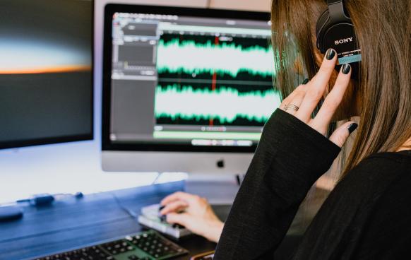 Photo of a woman editing audio and listening on headphones (Photo by Kelly Sikkema on Unsplash)